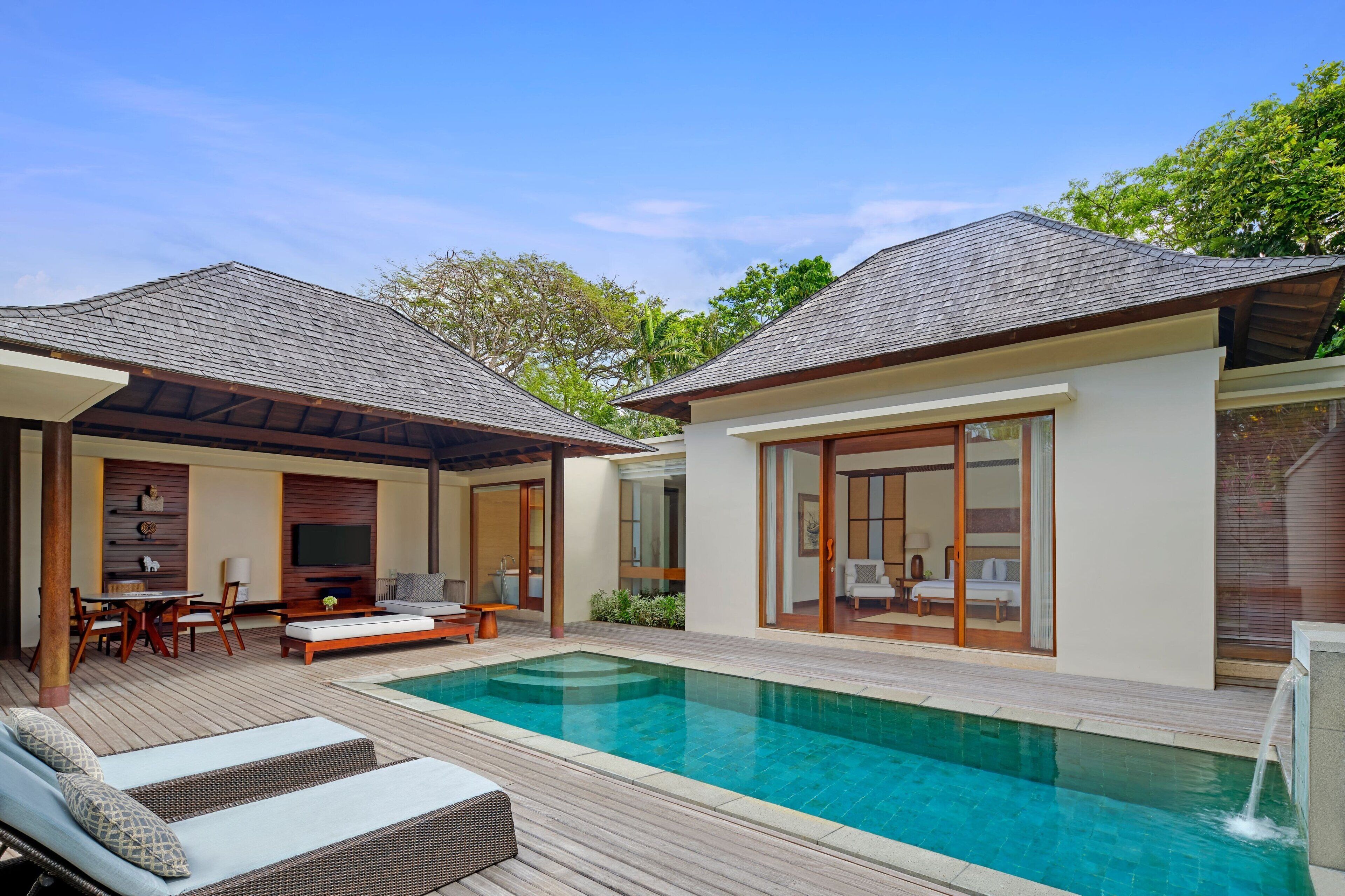 A modern outdoor pool area with a wooden deck, lounge chairs, and a covered seating area.
