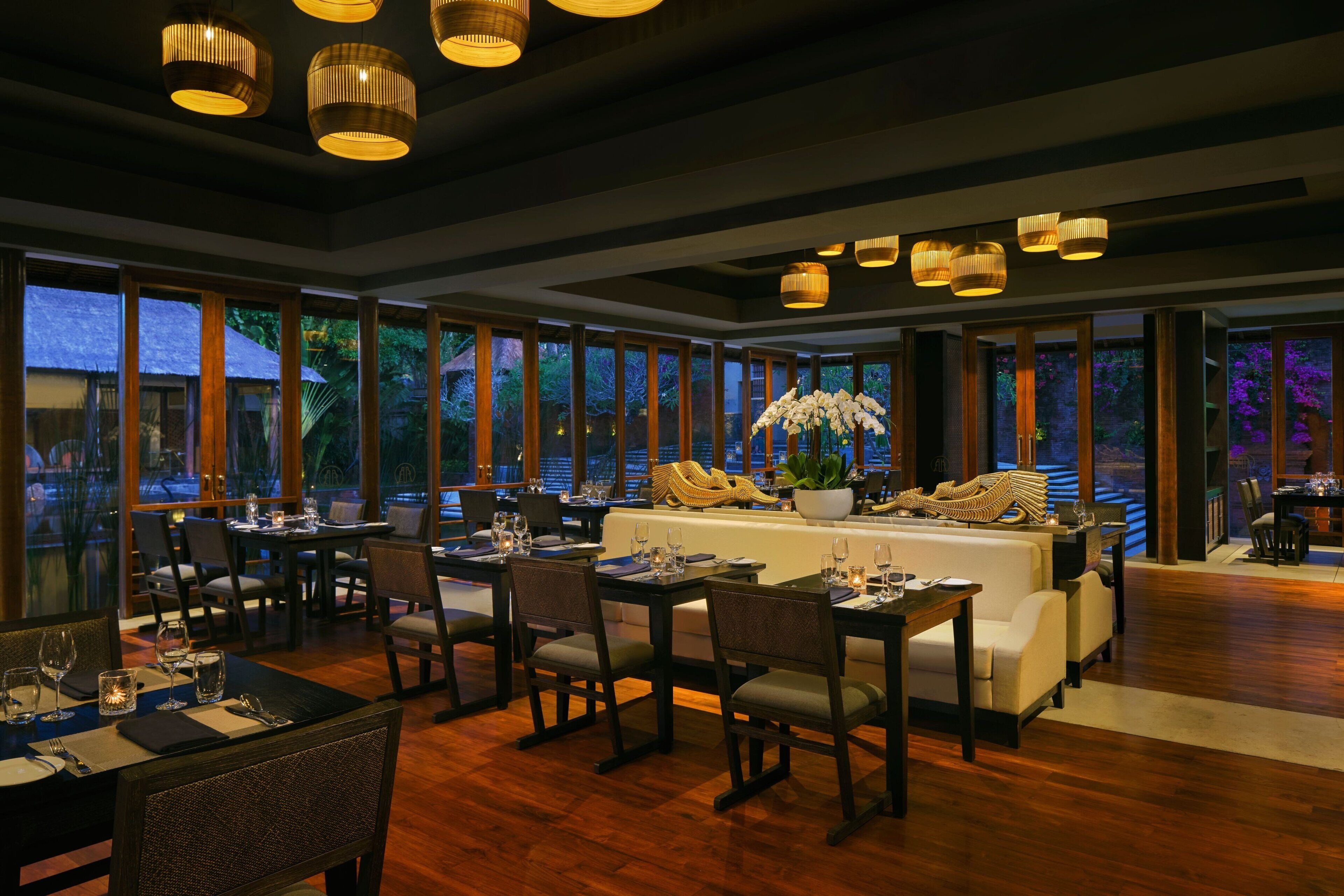 A restaurant with wooden flooring, large windows, and a central seating area with a sofa and chairs.