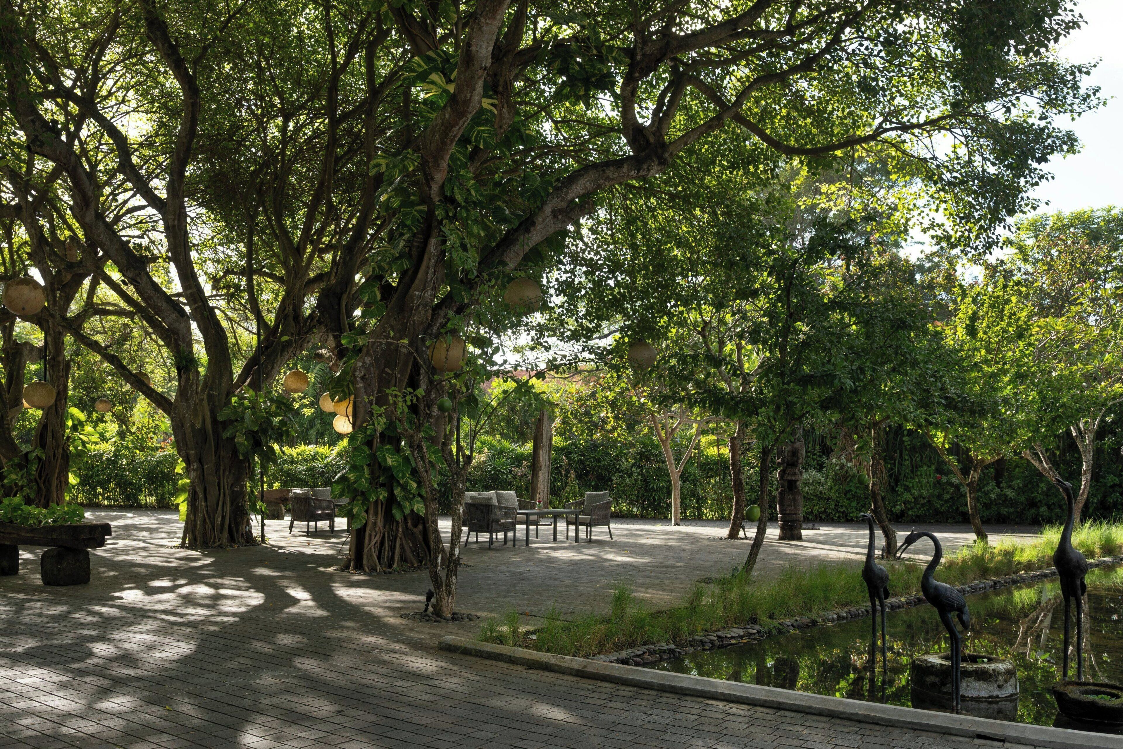 Un jardín tranquilo con un sendero empedrado, zonas de estar y un estanque con esculturas de aves.