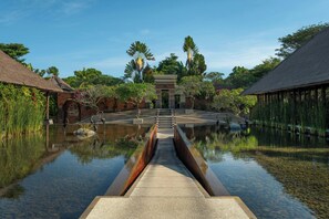 A tranquil waterway leading to a traditional building with a thatched roof, surrounded by lush greenery and a clear sky. - Amarterra Villas Resort Bali Nusa Dua, Autograph Collection (Nusa Dua)