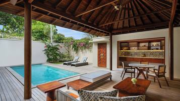 Uma área externa coberta com piscina, espreguiçadeiras, mesa de madeira e um espaço de estar com cadeiras e uma pequena mesa.