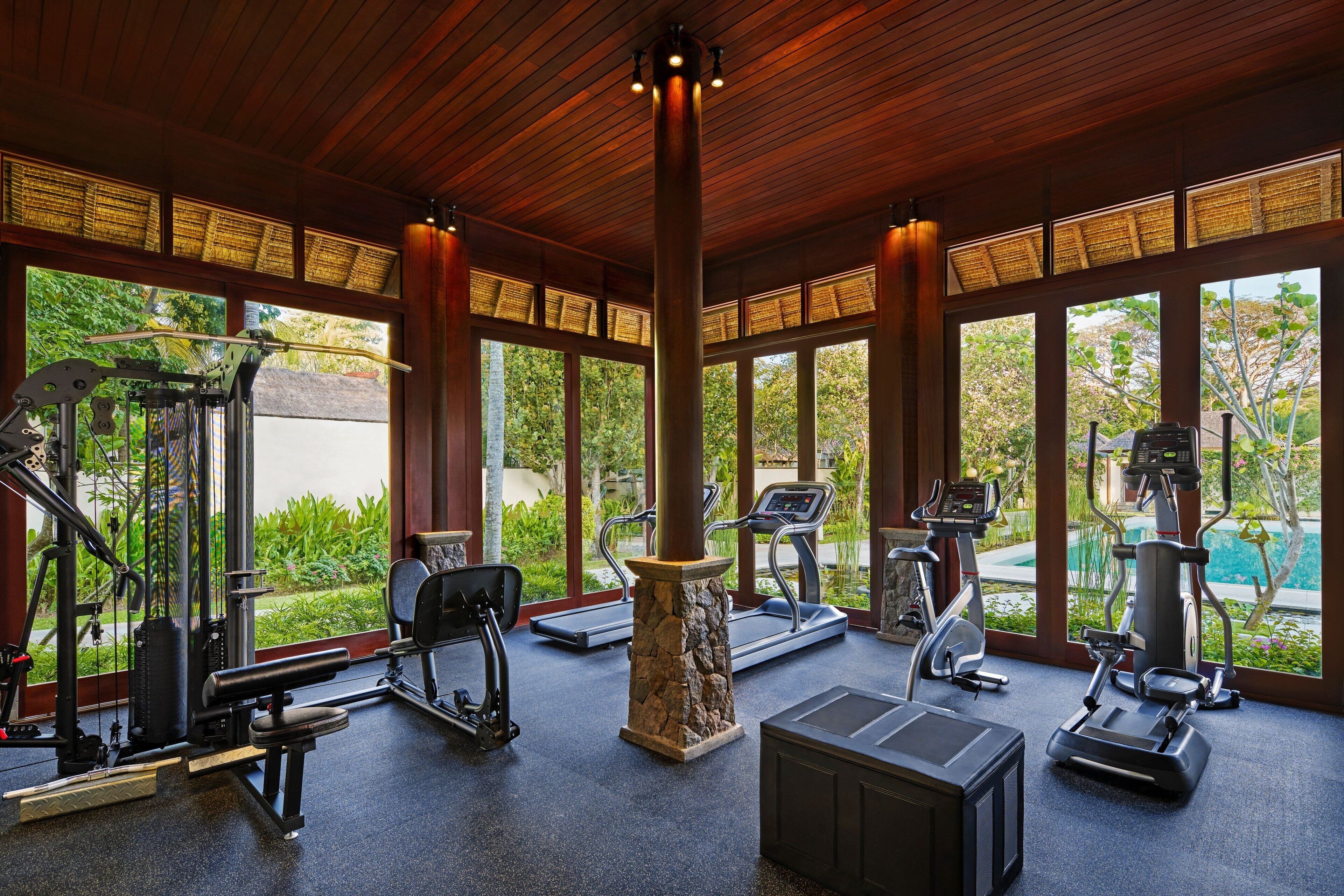 A gym with various exercise equipment, large windows, and a view of a swimming pool.