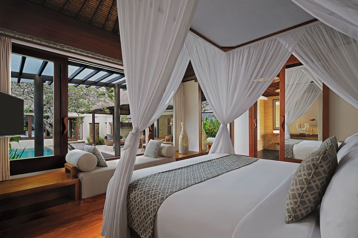 Ein Schlafzimmer mit einem großen Bett, einem weißen Baldachin, Holzböden und Blick auf einen Pool und eine Sitzgelegenheit im Freien.