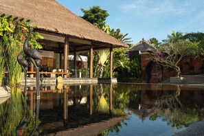 A tranquil pool area with a thatched-roof structure, a stone bridge, and lush tropical vegetation. - Amarterra Villas Resort Bali Nusa Dua, Autograph Collection (Nusa Dua)