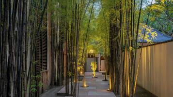 A bamboo-lined pathway leading to a building with a thatched roof.
