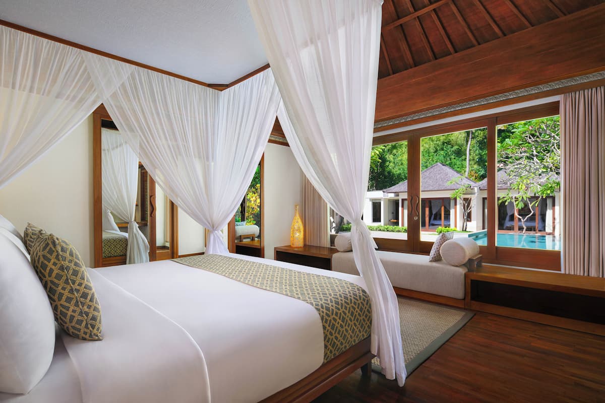 Ein Schlafzimmer mit einem großen Bett, Baldachin und Blick auf Pool und Grünflächen.