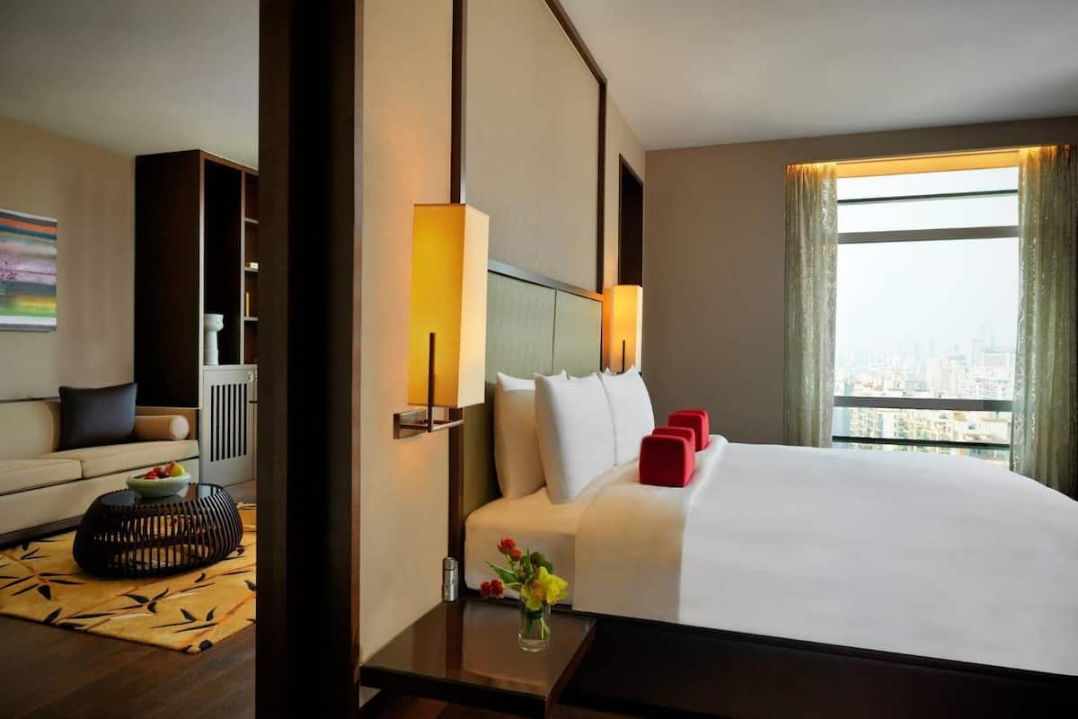 A hotel room with a large bed, a sofa, a small table with a vase, and a window with a city view.