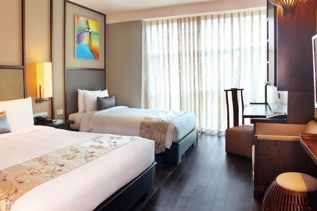 A hotel room with two beds, a desk, a chair, and a large window with curtains.