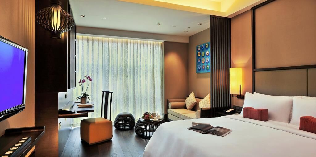 A hotel room with a bed, a TV, a sofa, a desk, and a window with curtains.
