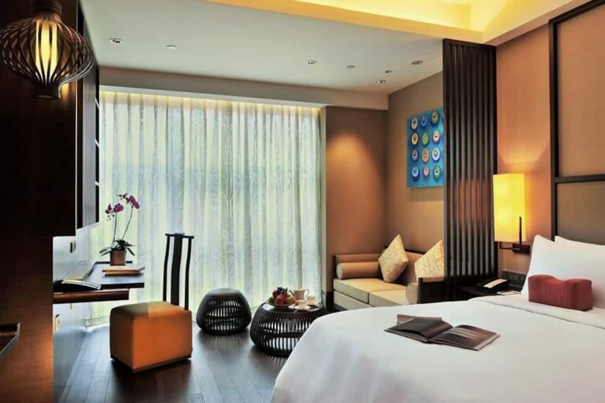 A hotel room with a bed, a TV, a sofa, a desk, and a window with curtains.