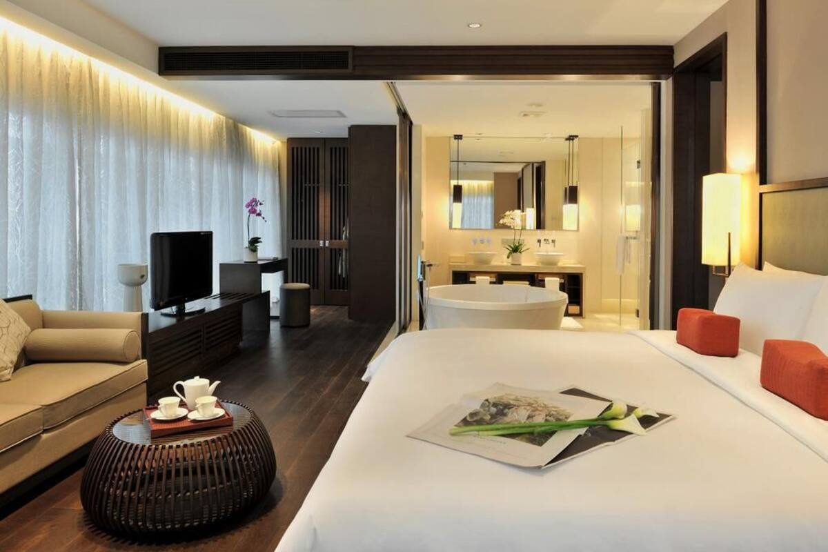 A modern hotel room with a bed, a sofa, a TV, a bathroom, and a dining area.