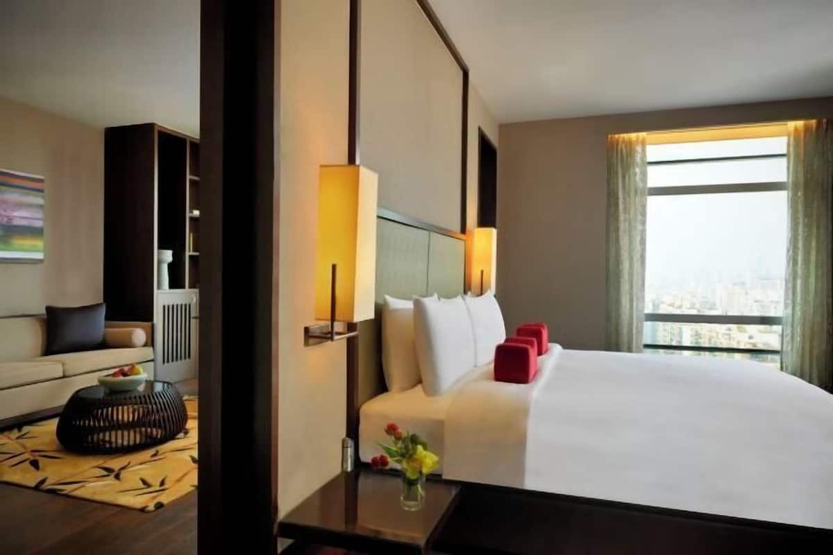 A hotel room with a bed, bedside tables, a sofa, a window with curtains, and a view of the city.