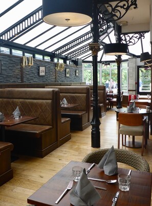 Ein Restaurant mit Holzbänken und -tischen, einer Steinwand und Blick ins Freie.