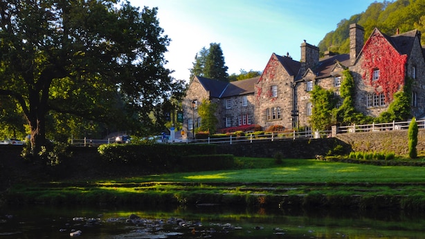 A stone building with a traditional design, featuring multiple chimneys and a prominent red ivy-covered section. - Royal Oak Hotel (Betws-Y-Coed)