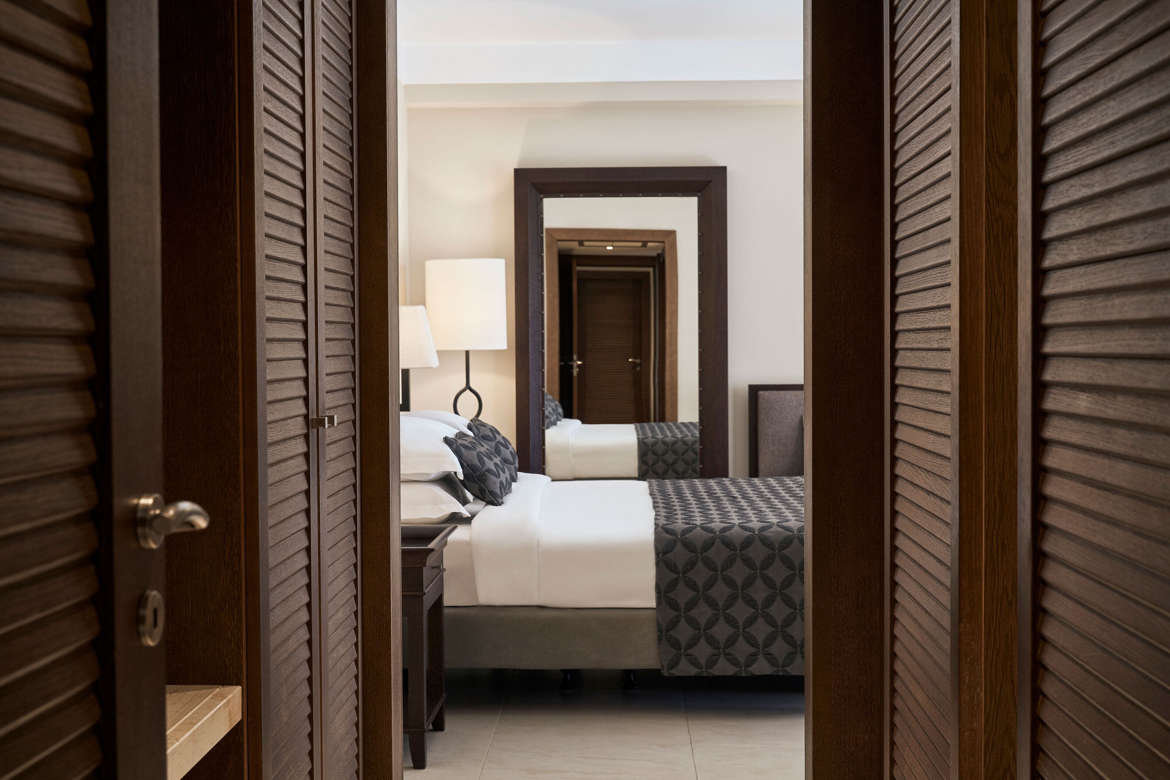 Una habitación de hotel con cama, mesita de noche, lámpara y espejo.
