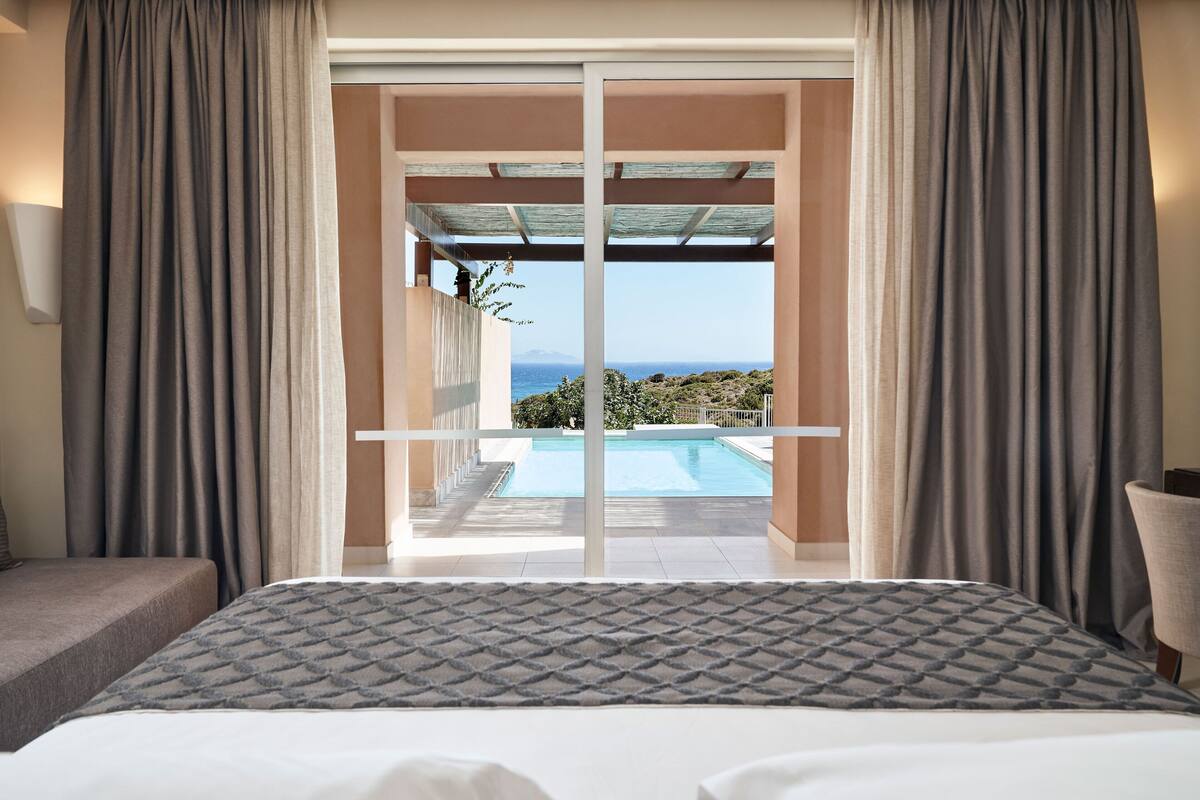 Ein Schlafzimmer mit einem großen Bett, Blick auf einen Pool und einem Balkon mit Meerblick.