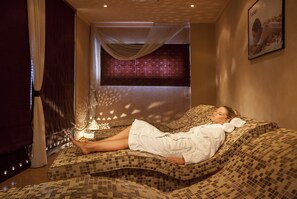 Une personne allongée sur une table de massage à motifs dans une pièce dotée d’une grande fenêtre et d’un tableau accroché au mur.