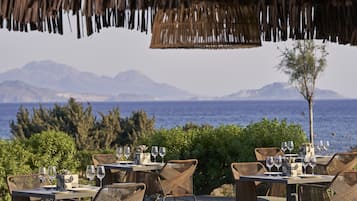 Un espacio de comedor al aire libre con mesas y sillas, con vistas a un cuerpo de agua y montañas.