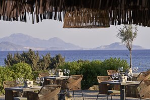 Un espacio de comedor al aire libre con mesas y sillas, con vistas a un cuerpo de agua y montañas.