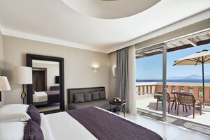 A hotel room with a bed, a sofa, a table with fruit, and a balcony with a table and chairs.