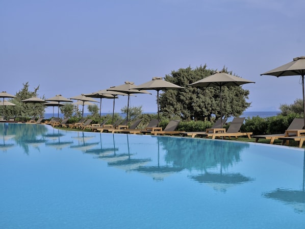 A poolside area with lounge chairs and umbrellas, surrounded by trees and a clear sky.
