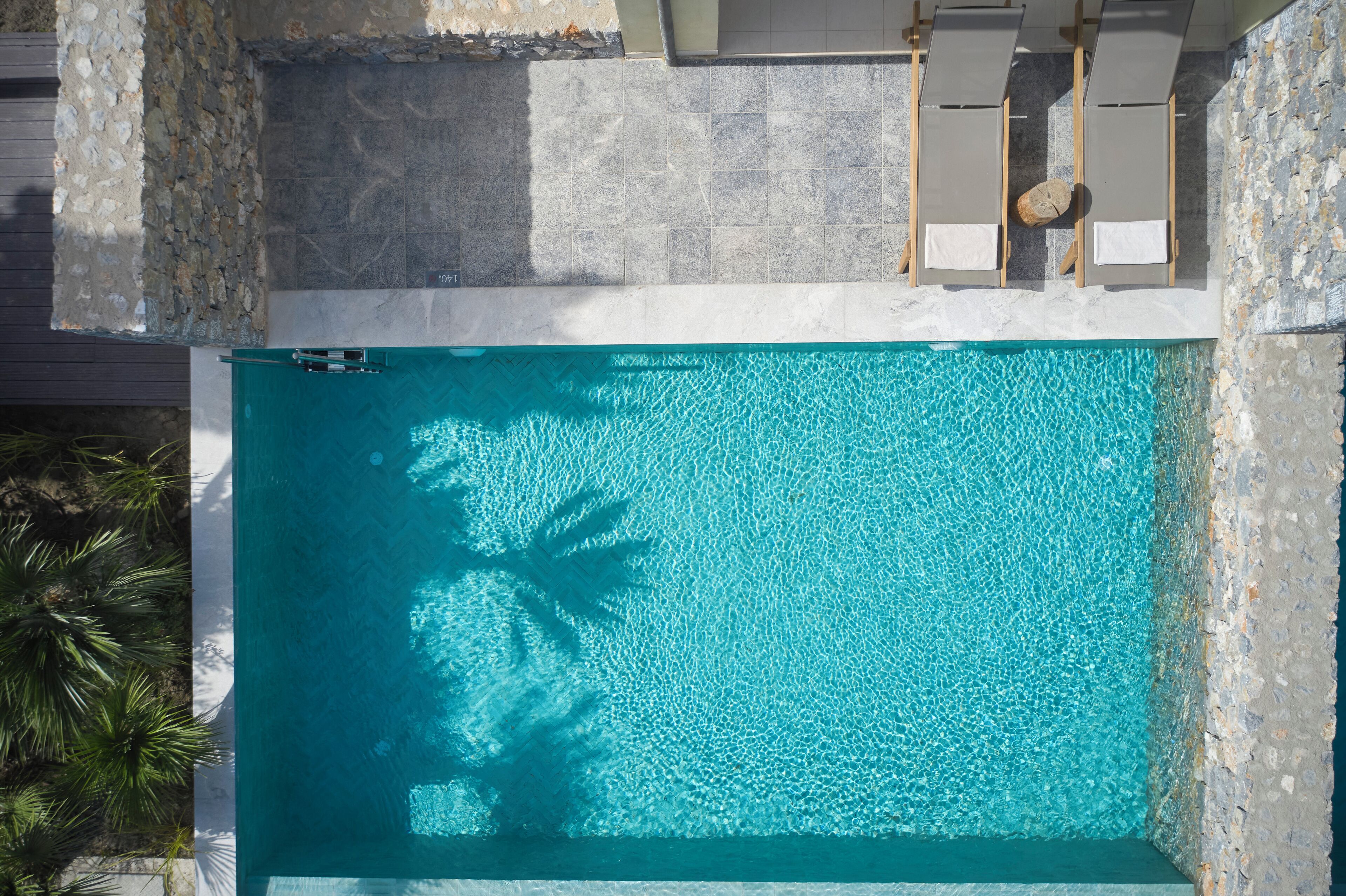 Ein rechteckiger Swimmingpool mit klarem, blauem Wasser, umgeben von Steinmauern und Holzliegen.