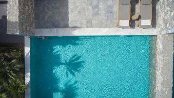 Ein rechteckiger Swimmingpool mit klarem, blauem Wasser, umgeben von Steinmauern und Holzliegen.