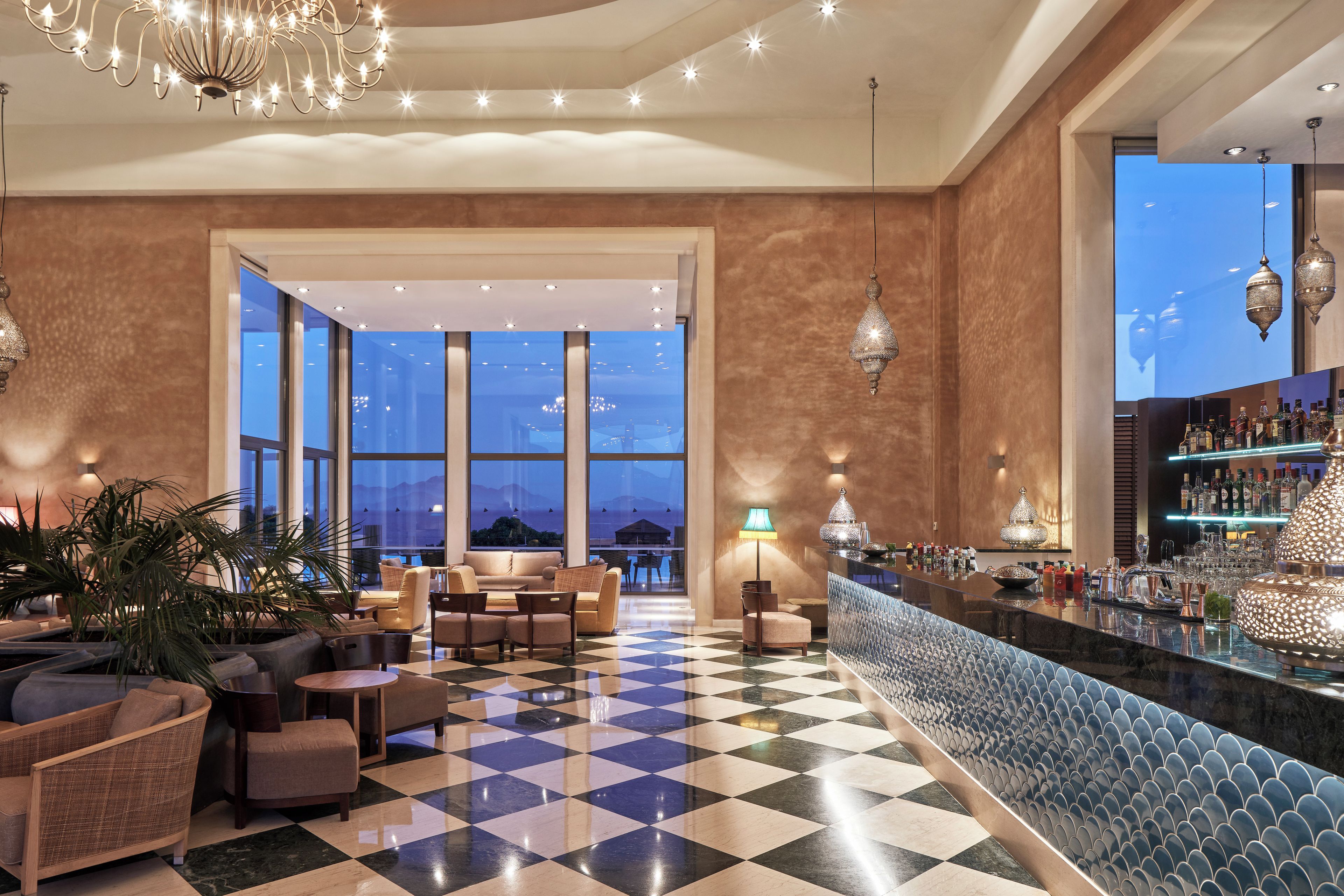 Hall d'albergo con pavimento a scacchi, zona salotto, bar e ampie finestre con vista.