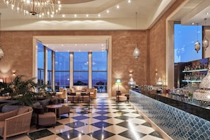 A hotel lobby with a checkered floor, seating area, bar, and large windows offering a view.