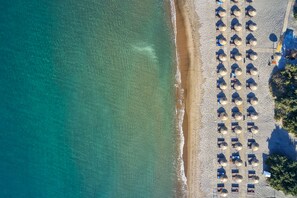 An aerial view of a beach with rows of umbrellas and lounge chairs, indicating a resort setting.