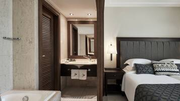 A hotel room with a large bed, a bedside table, a nightstand, a bathroom with a bathtub, and a mirror.