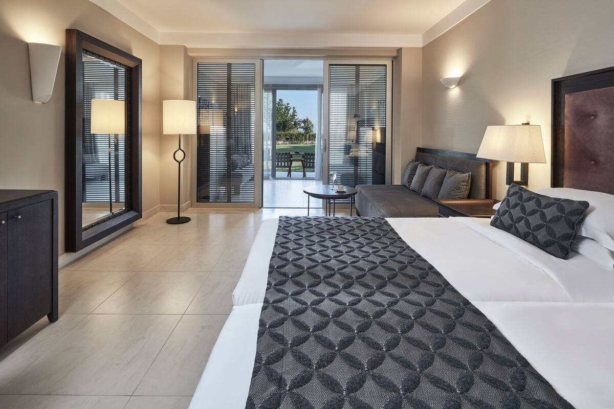 Ein Hotelzimmer mit einem großen Bett, einem Schreibtisch, einem Stuhl und Blick ins Freie durch die Schiebetüren.