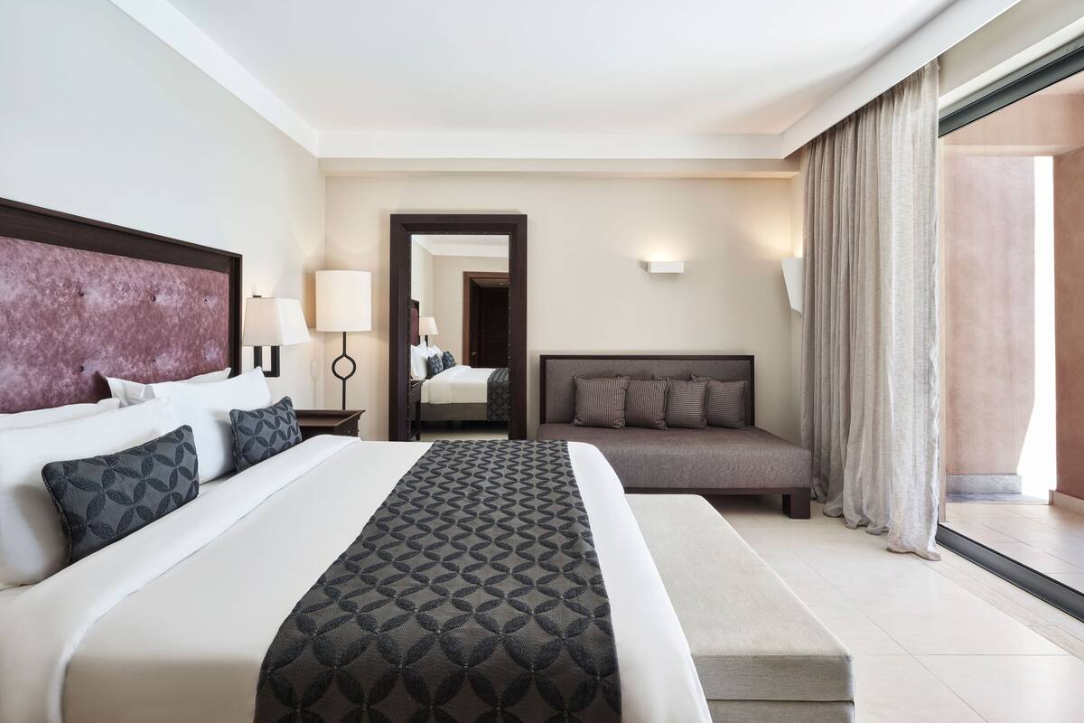Ein Hotelzimmer mit einem großen Bett, einer Couch, einem Schreibtisch und einem durchgegangene Tür erkennbaren Badezimmer.