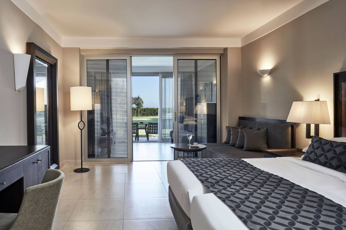 Ein Hotelzimmer mit Bett, Schreibtisch, Stuhl, Tisch und einem Balkon mit Blick.