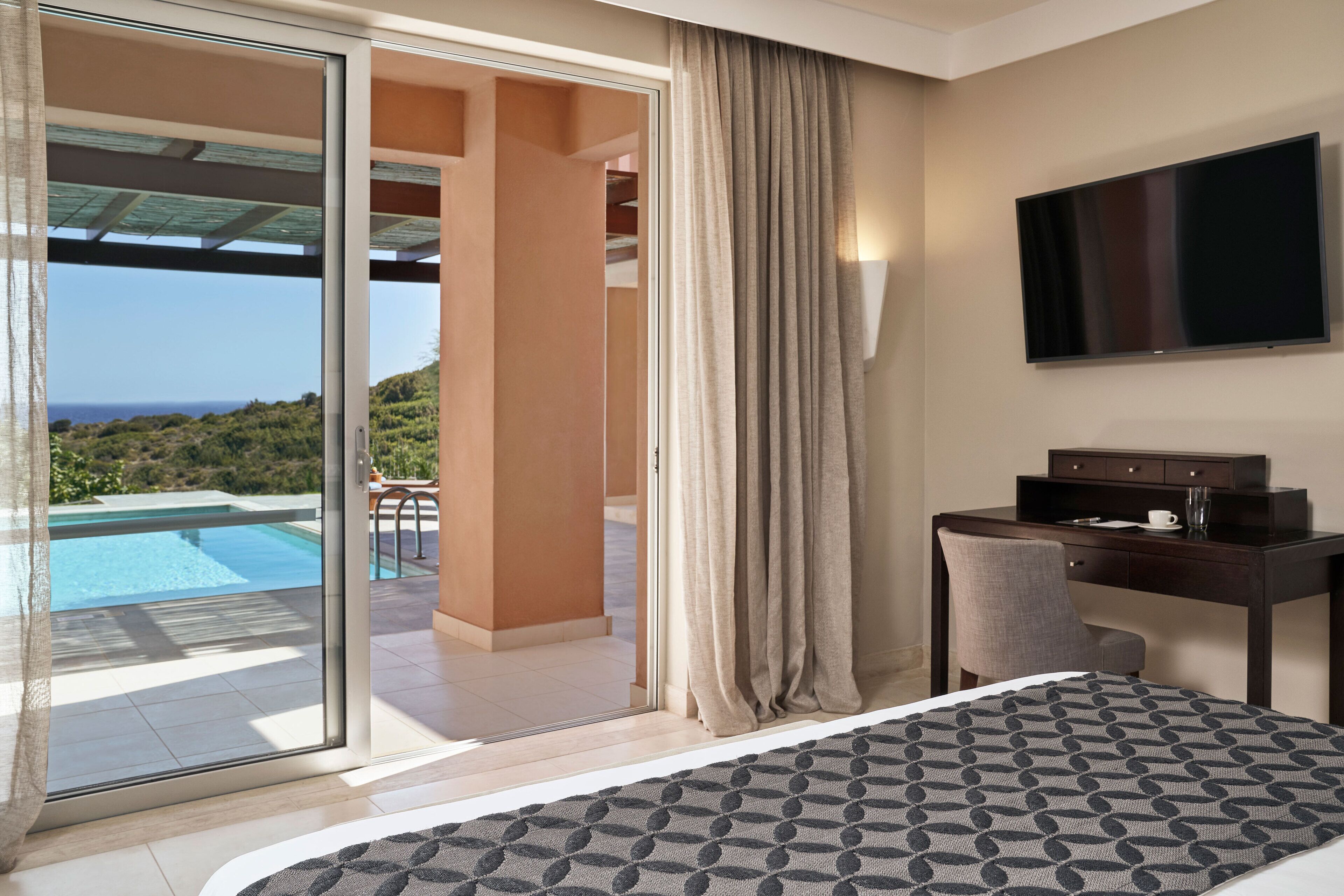 Ein Hotelzimmer mit Bett, Schreibtisch, Fernseher und Blick auf Pool und Landschaft.