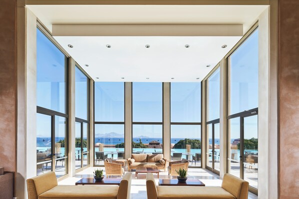 Una habitación amplia con ventanas grandes, un sofá, una mesa de centro y vista al mar.