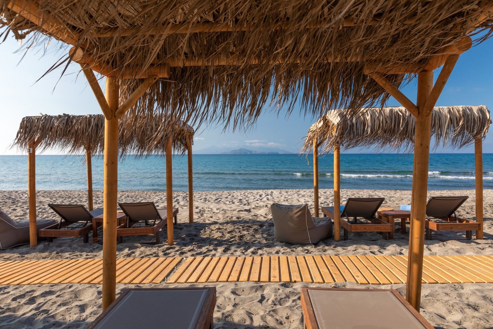 Una spiaggia con lettini di legno e una struttura con tetto di paglia.