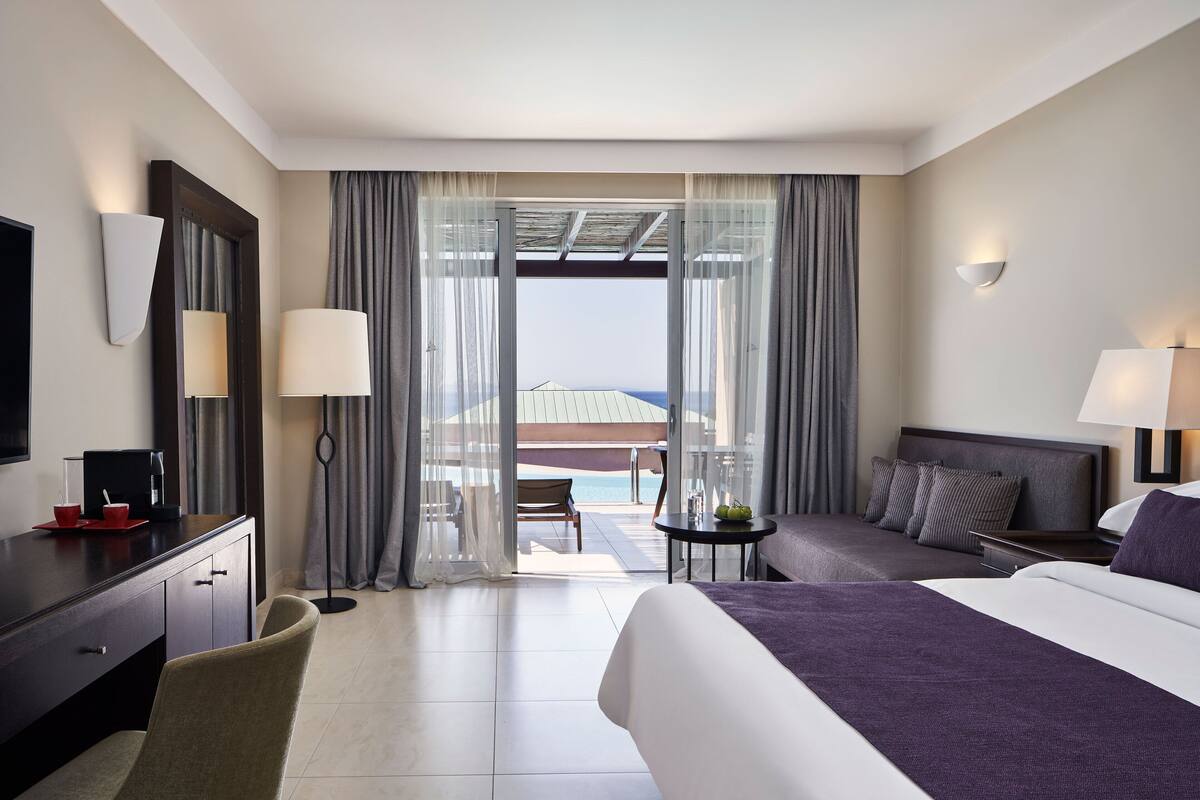 Ein Hotelzimmer mit Bett, Schreibtisch, Stuhl, einem kleinen Tisch und Blick auf den Ozean.