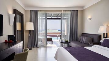 Habitación de hotel con cama, escritorio, silla, una mesita y vista al océano.