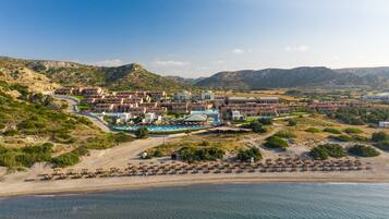 A coastal resort with multiple buildings, a swimming pool, and a beach area with umbrellas.