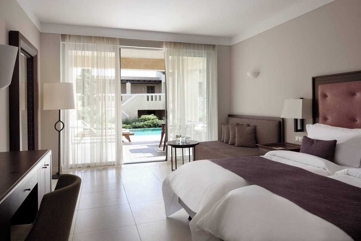Ein Hotelzimmer mit Bett, Nachttischen, einem Schreibtisch und Blick auf einen Pool und eine Außenbereich-Sitzgelegenheit.