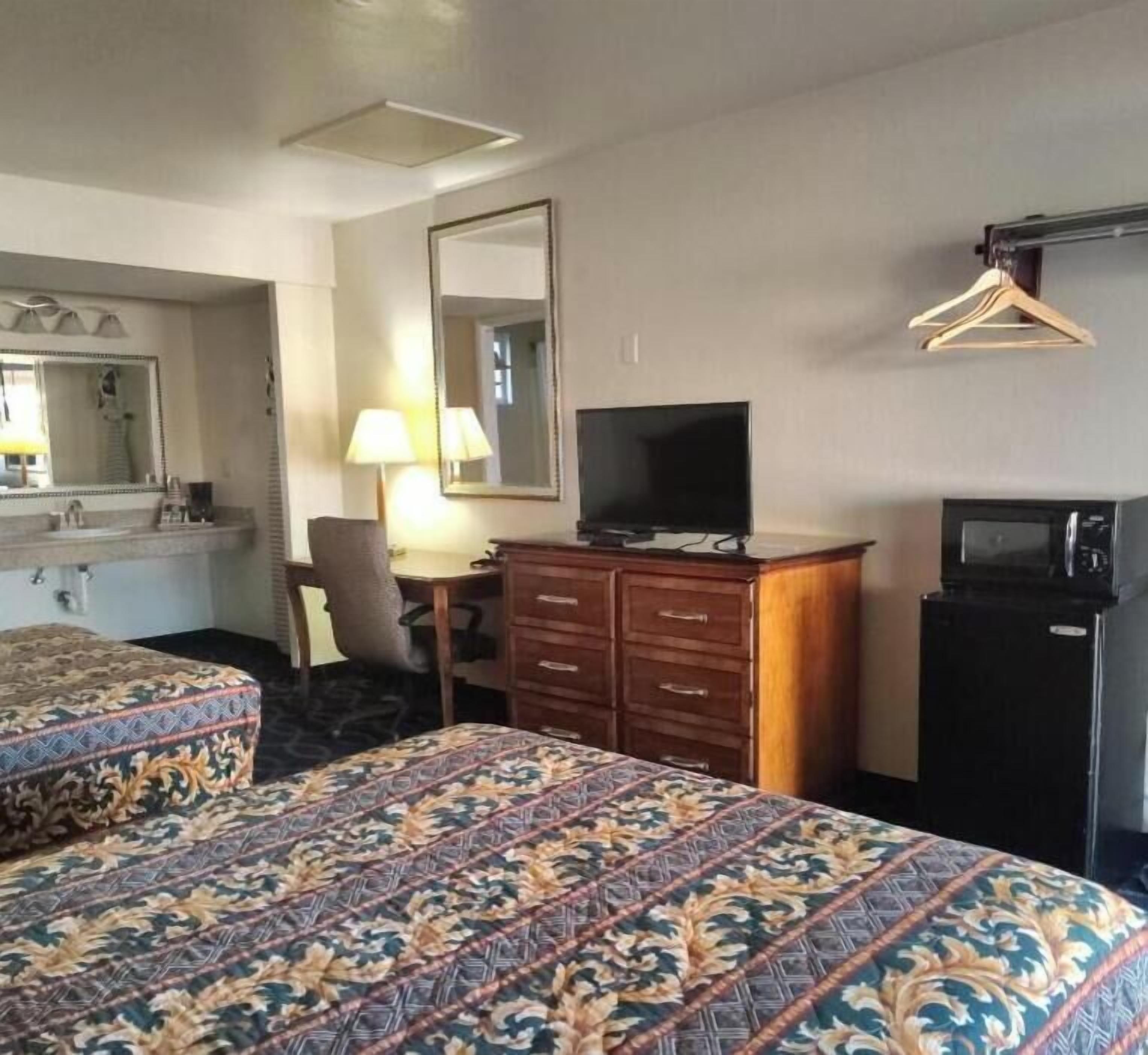 Habitación de hotel con dos camas, un escritorio con televisor, cómoda, espejo y perchero.