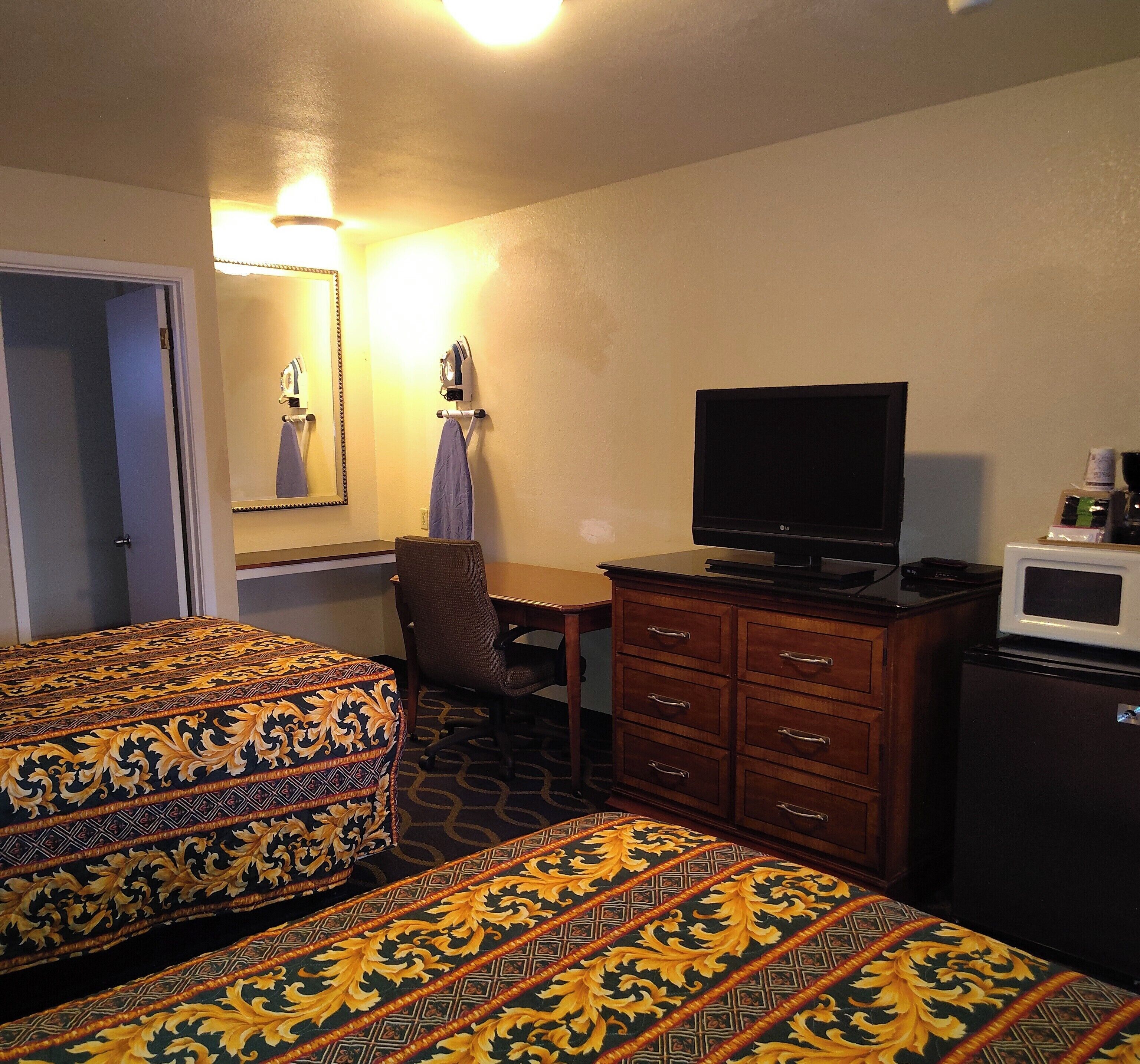 A hotel room with two beds, a television, a dresser, and a microwave.