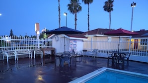 A swimming pool with a tiled edge, surrounded by outdoor furniture and palm trees. - Holiday Motel Oakdale (Oakdale)