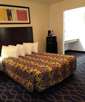 A hotel room with a bed, pillows, a coffee maker, and a framed picture on the wall. - Holiday Motel Oakdale (Oakdale)