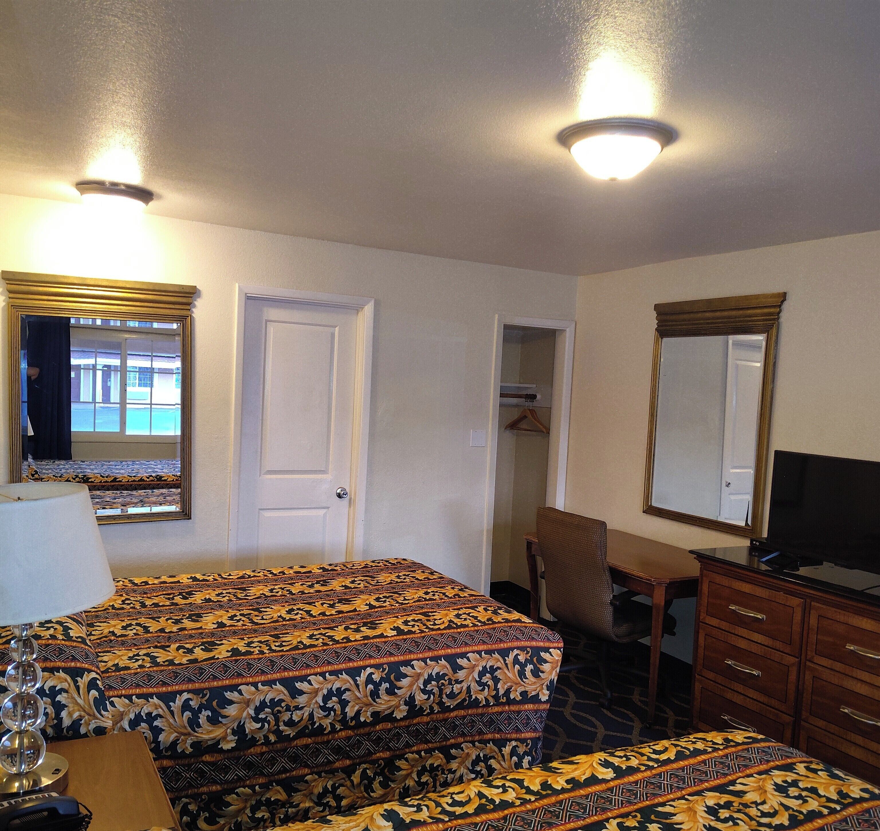 Une chambre d’hôtel avec un lit, un bureau, une télévision et un miroir.