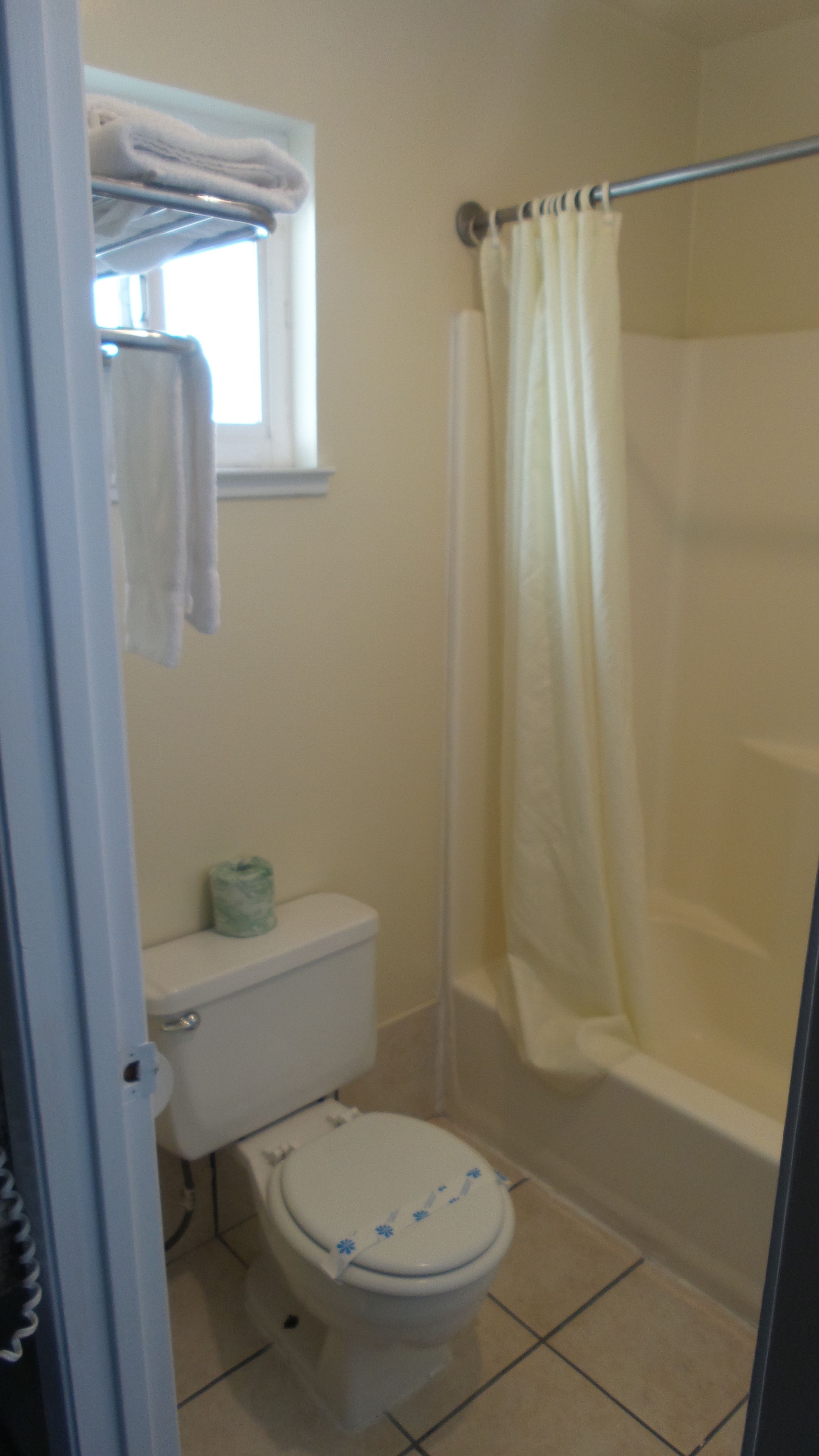 A bathroom with a toilet, a shower with a curtain, and a window above the toilet.