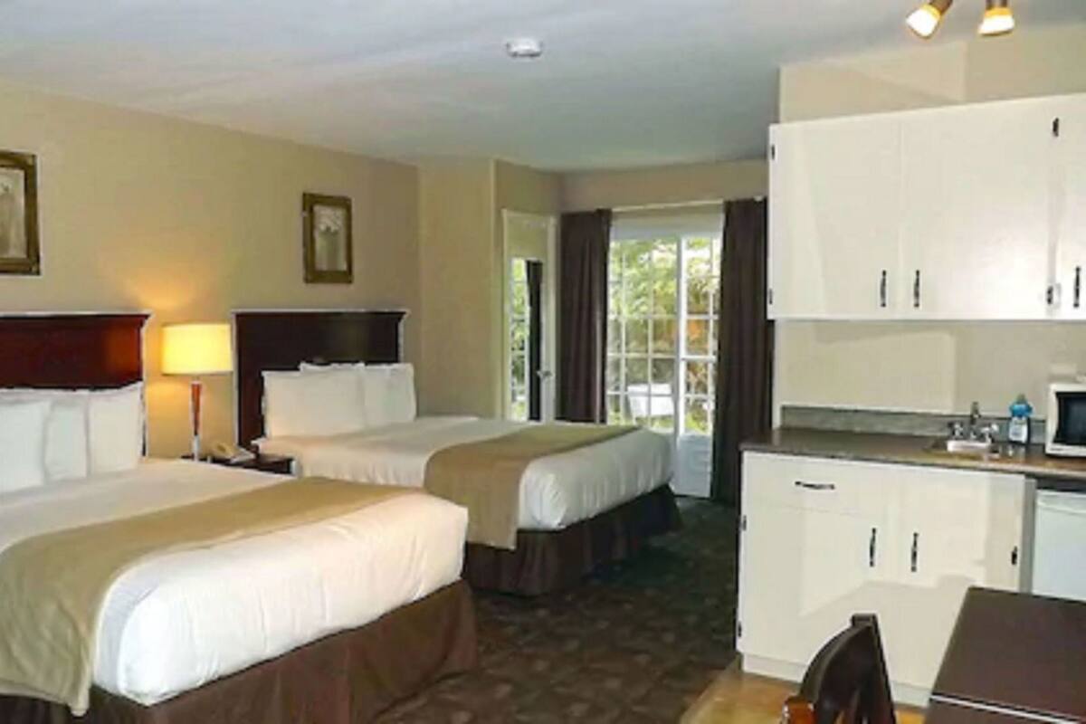 Une chambre d’hôtel avec deux lits, un bureau, une chaise, une lampe et une fenêtre.