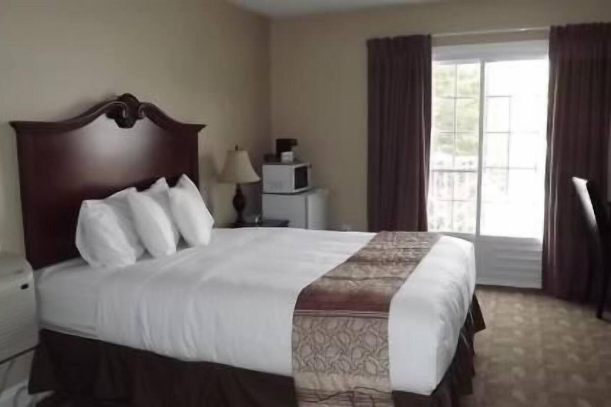 Une chambre d’hôtel avec un grand lit, un bureau, une chaise, une lampe et une fenêtre avec des rideaux.