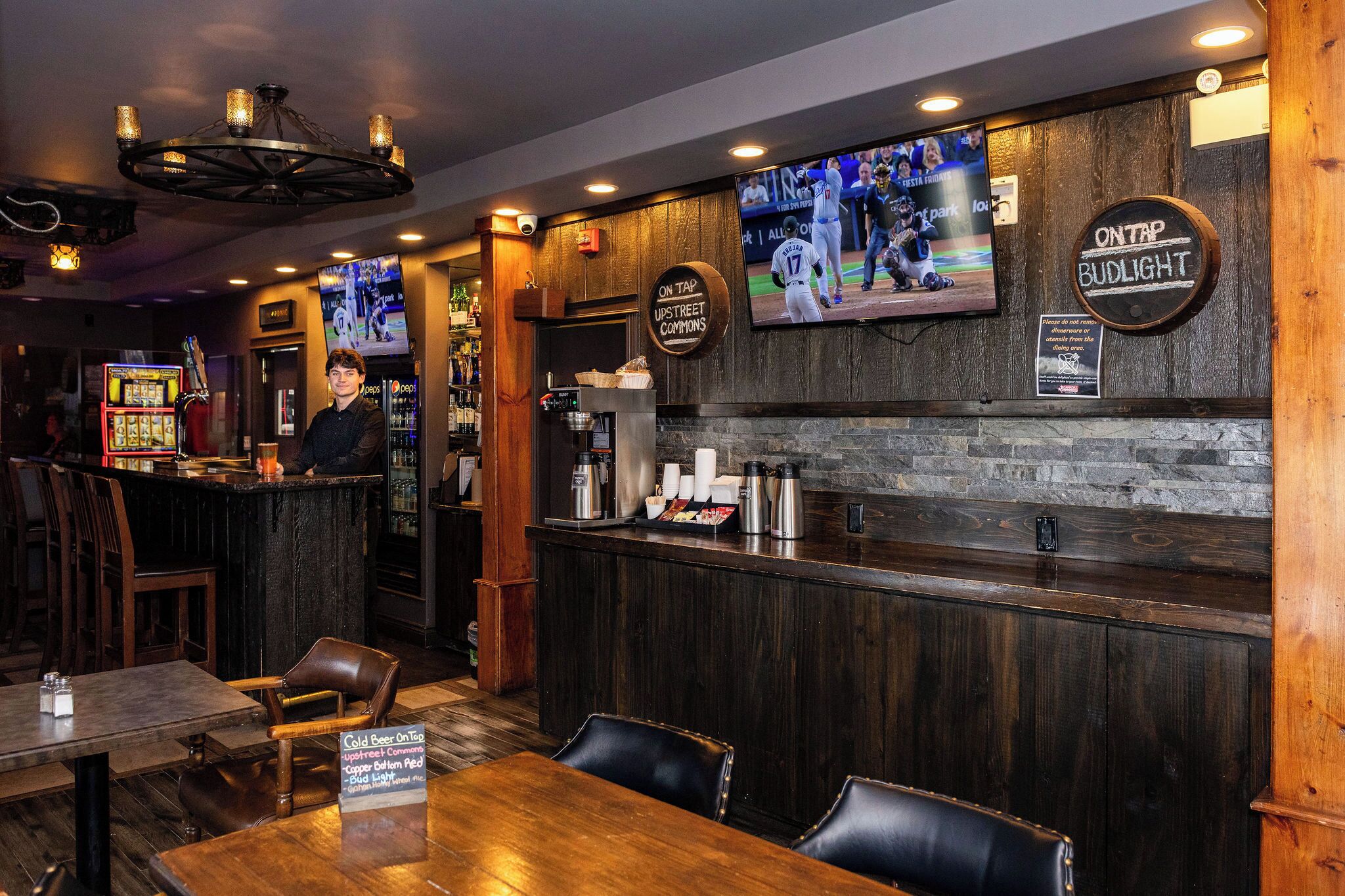 Un espace bar avec un comptoir en bois, un téléviseur fixé au mur et un panneau indiquant « BUDLIGHT À LA POMPE ».